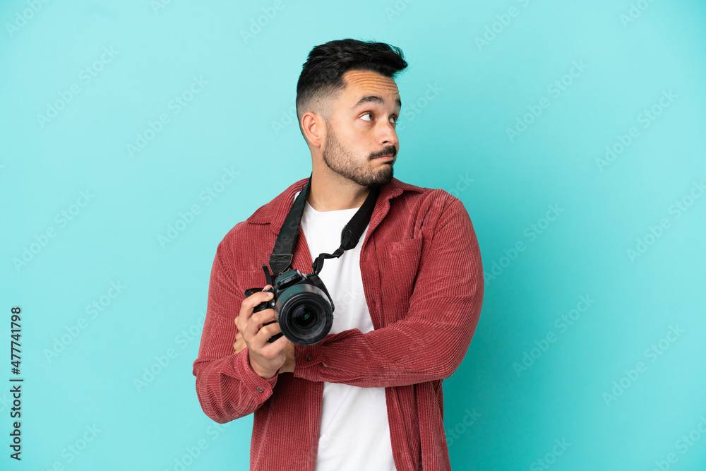 Young photographer caucasian man isolated on blue background making doubts gesture while lifting the shoulders Young photographer caucasian man isolated on blue background making doubts gesture while lifting the shoulders