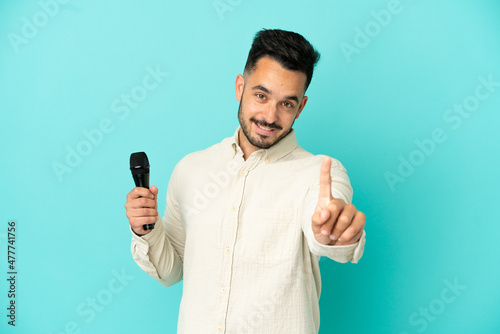 Young caucasian singer man isolated on blue background showing and lifting a finger