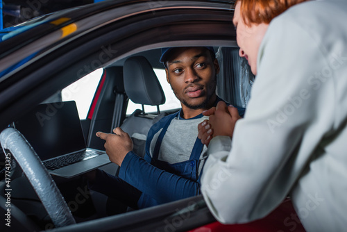 african american technician pointing at laptop while sitting in car near blurred customer. © LIGHTFIELD STUDIOS
