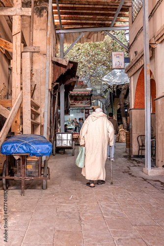 Fes, Morocco. October 10, 2021. Rear view of senior old man walking with stick on street against restaurant