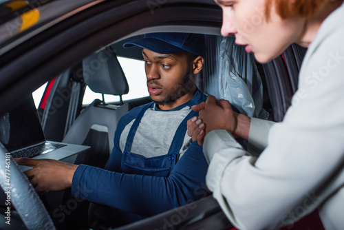 african american foreman pointing at laptop while sitting in car of blurred client.