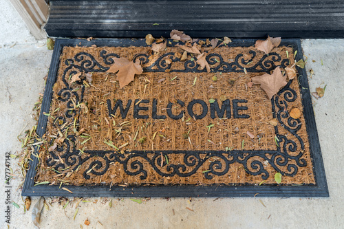 Welcome mat with autumn leaves outside suburban front door.