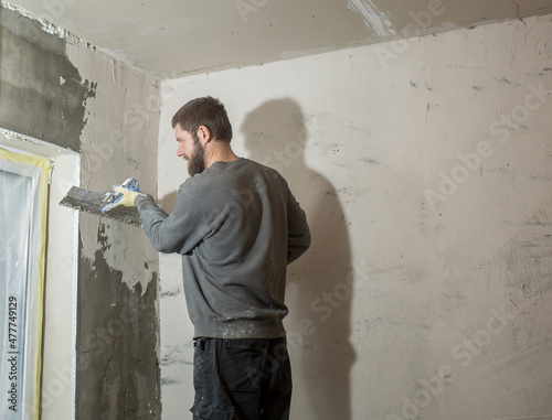 a male plasterer with a beard plasters a concrete wall with a spatula. © Olga