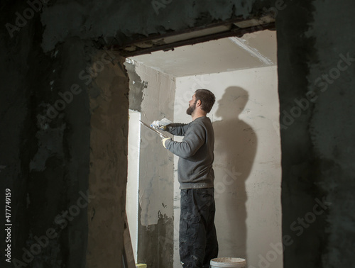 a male plasterer with a beard plasters a concrete wall with a spatula.. © Olga
