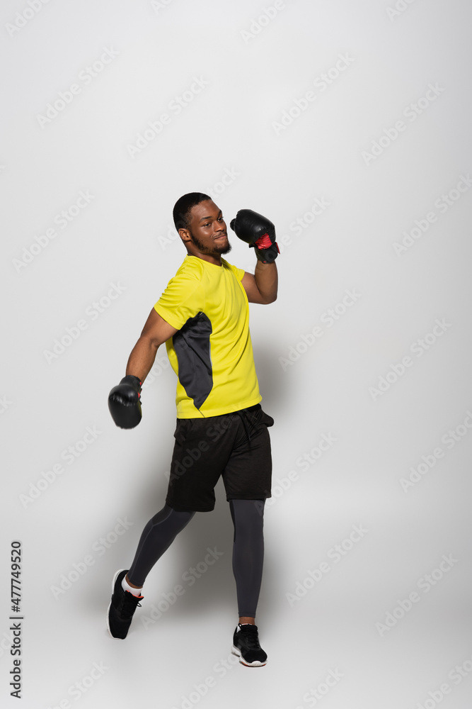 full length of strong african american sportsman in boxing gloves jumping on grey. full length of strong african american sportsman in boxing gloves jumping on grey.