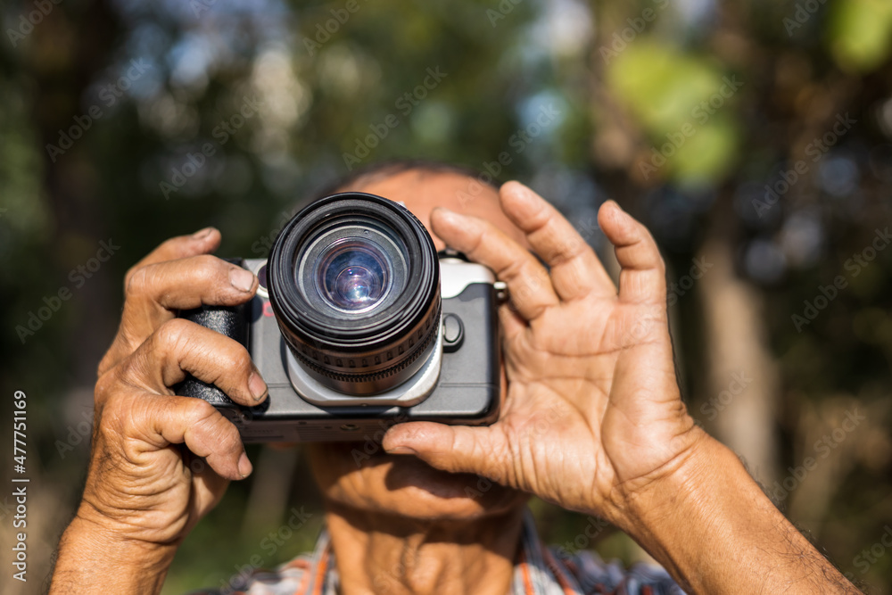 Close-up view of both hands of an elderly Thai man holding a film camera. Close-up view of both hands of an elderly Thai man holding a film camera.