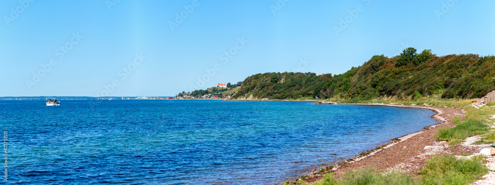 Obraz premium Panorama of the coast of Ven, an island of the coast of Landskrona, Sweden. Calm summer sea, blue water and sky. Sunlit coastline on the other side. Beach with trees and gravel