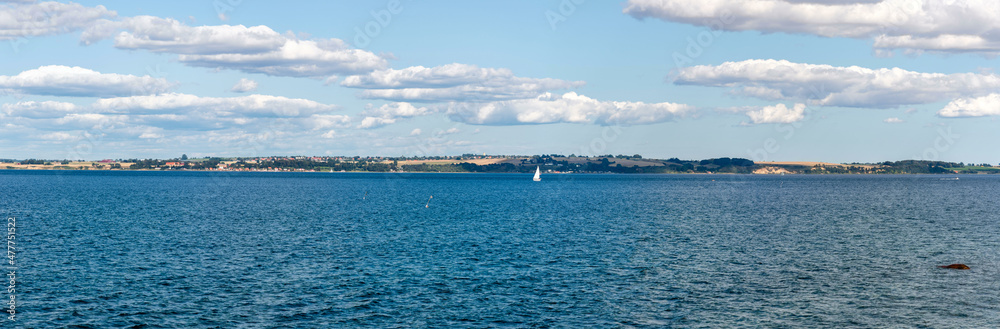 Panorama of the coast of Ven, an island of the coast of Landskrona, Sweden. Calm summer sea, blue water and sky. Sunlit coastline on the other side. Beach with trees and gravel