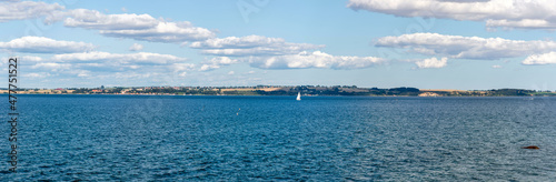 Panorama of the coast of Ven  an island of the coast of Landskrona  Sweden. Calm summer sea  blue water and sky. Sunlit coastline on the other side. Beach with trees and gravel
