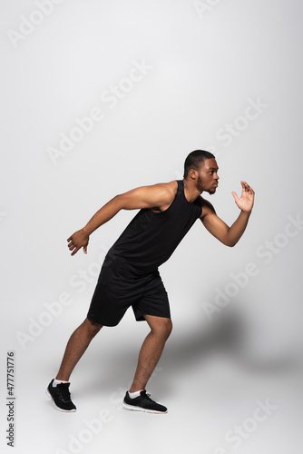 full length of young african american sportsman running fast on grey.