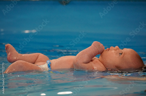 A baby floats on its back in a pool. First time swimming. High quality photo