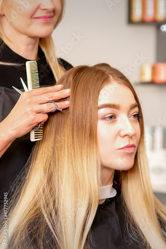 Gorgeous blonde long hair woman and her hairdresser looking and checking out hairstyle. Beautiful hairstyle of a young blonde woman after dying hair in a beauty salon, results of hair treatment