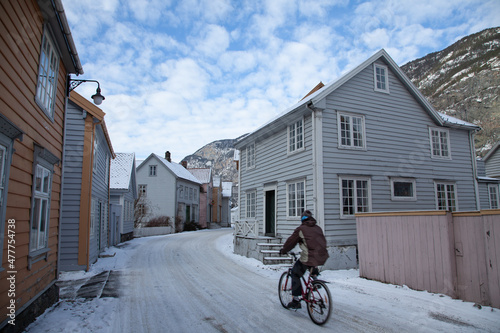 Person on bicycle driving on snow road in the middle of a village photo