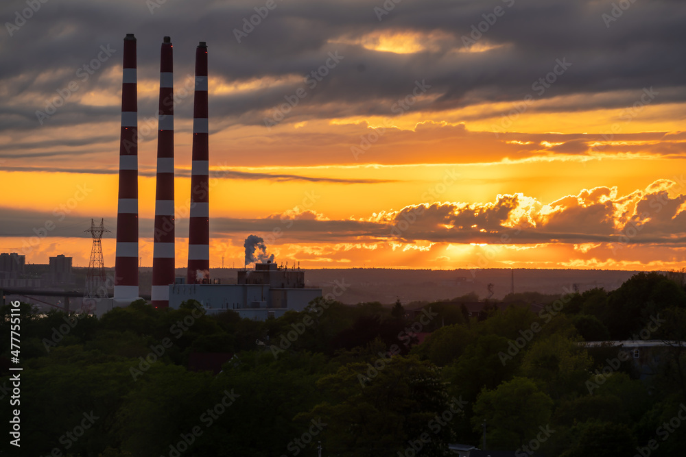 Power plant smoke stacks silhouetted against a dramatic sunset.