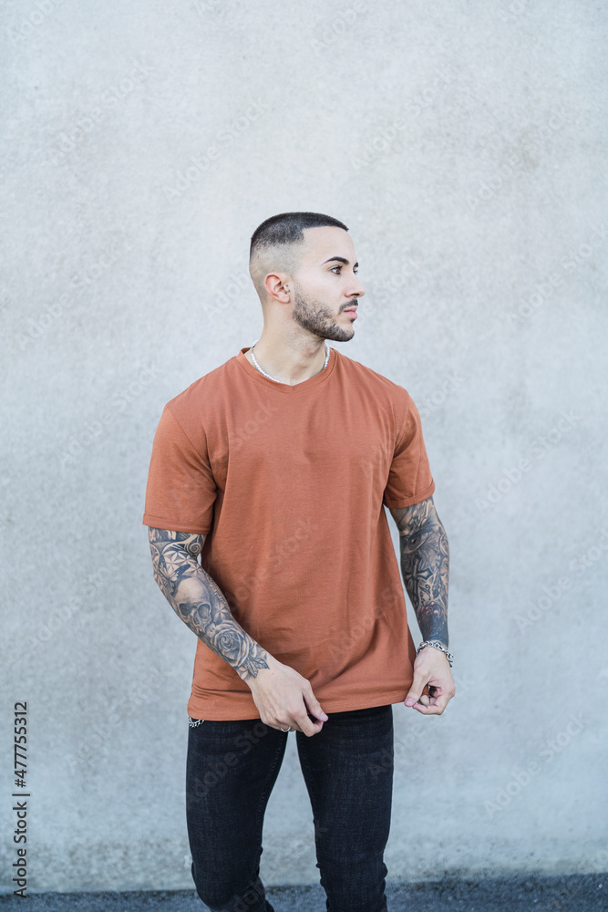 Chico joven tatuado posando con ropa urbana en la calle