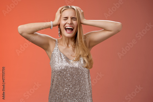 Upset distressed pressured fed up panicking young blond woman in dress scream cry heart out being heartbroken close eyes hold hands head mentaly unstable standing sad depressed red background photo