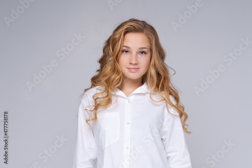 Caucasian girl, happy woman with blond long hair. In a white shirt. Makeup. The concept of people and emotions. Happy watching camera isolated on gray background