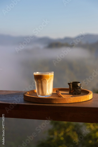 Sunrise coffee in nature. Dirty coffee on wooden table with mountain fog on shade of sunrise background. Good morning.