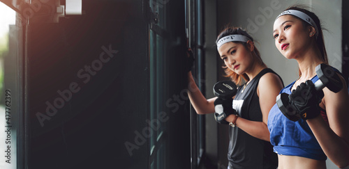 Two young sportwoman doing fitness exercise with dumbbells at gym. Sport background banner.