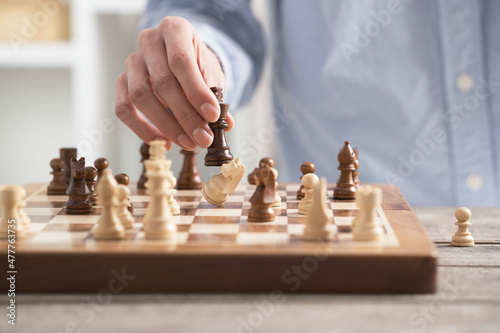 Girl player performs a knight chess piece move. On the chessboard there is a brown board made of natural wood. A female hand holds a horse figure. 
