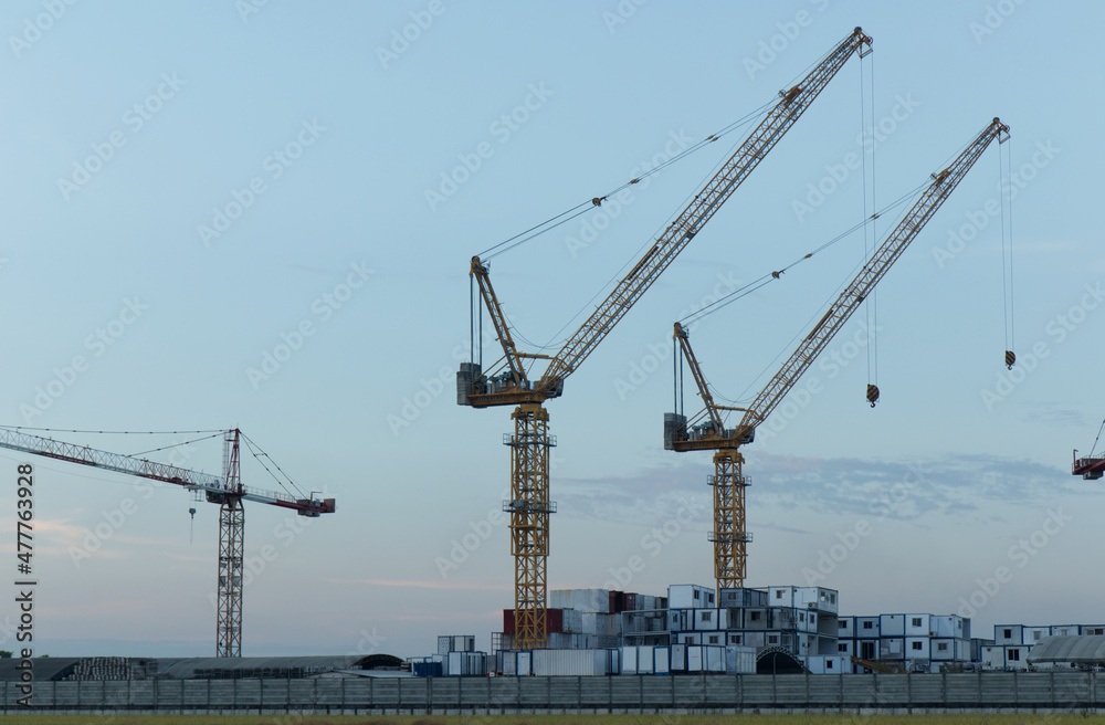 White containers, yellow steel tower cranes, near green fields, White containers, yellow steel tower cranes, near green fields,