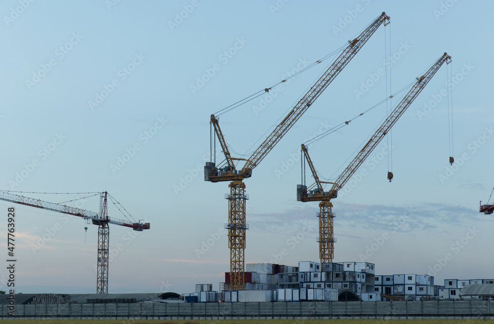 White containers, yellow steel tower cranes, near green fields,