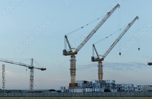 White containers, yellow steel tower cranes, near green fields,