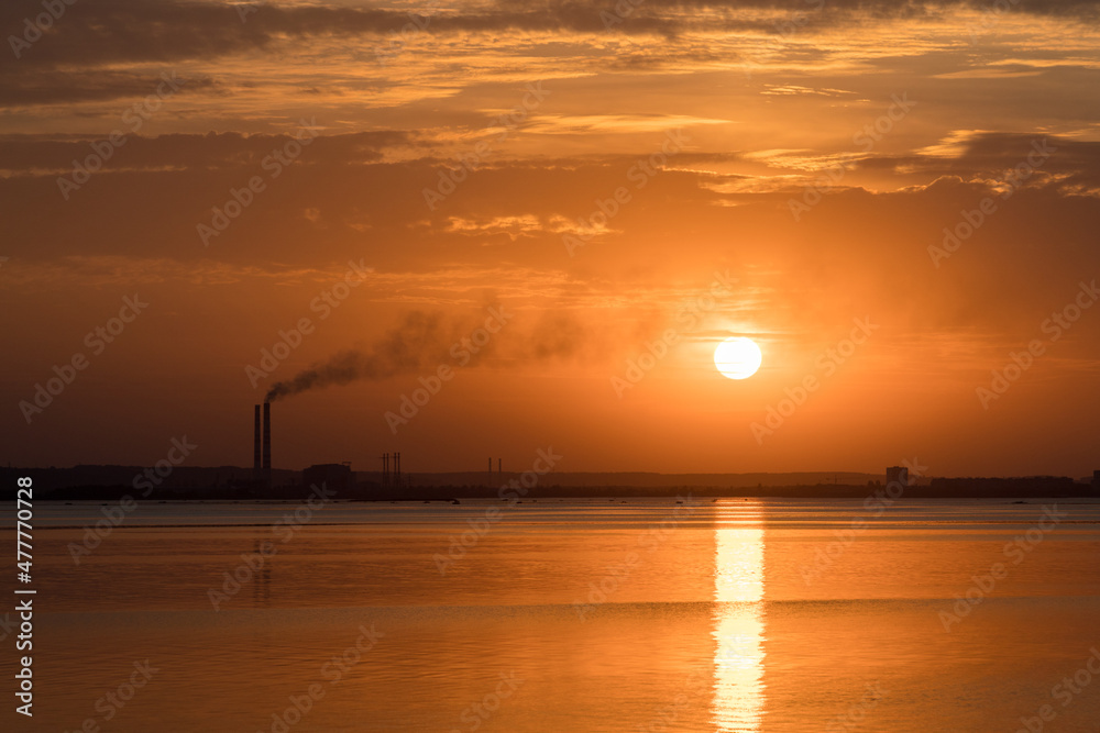 Sunset view of smoking industrial pipes on a horizon over the river.