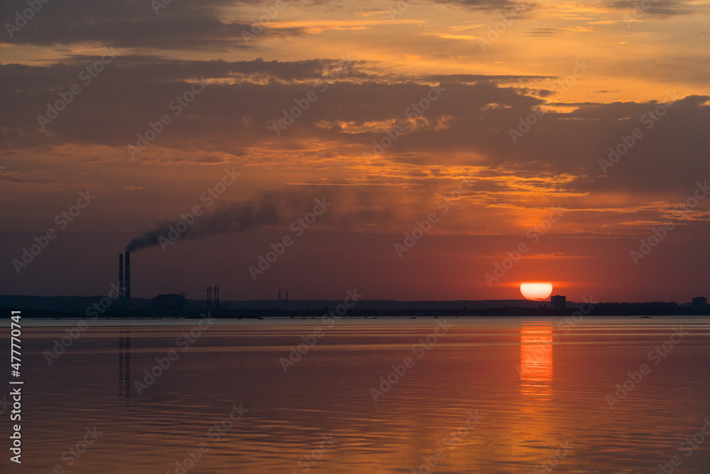 Sunset view of smoking industrial pipes on a horizon over the river.