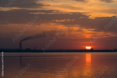 Sunset view of smoking industrial pipes on a horizon over the river.