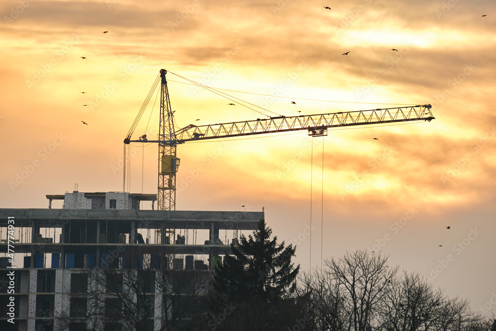 Dark silhouette of tower crane at high residential apartment buildings construction site at sunset. Real estate development