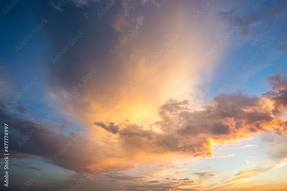 Dramatic cloudscape with puffy clouds lit by orange setting sun and blue sky