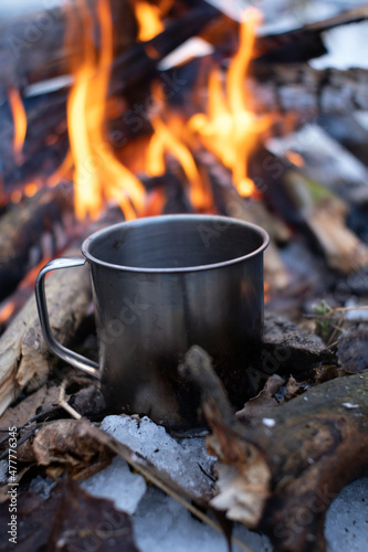 a mug stands on the wood near a fire in a snowy forest