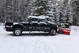 Black pickup truck with snow plow after snowstorm in rural setting in forest