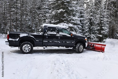 Black pickup truck with snow plow after snowstorm in rural setting in forest