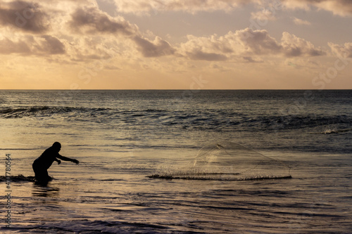 Silhouette of fisherman throwing his net at sunset in Fernando de Noronha, Brazil.