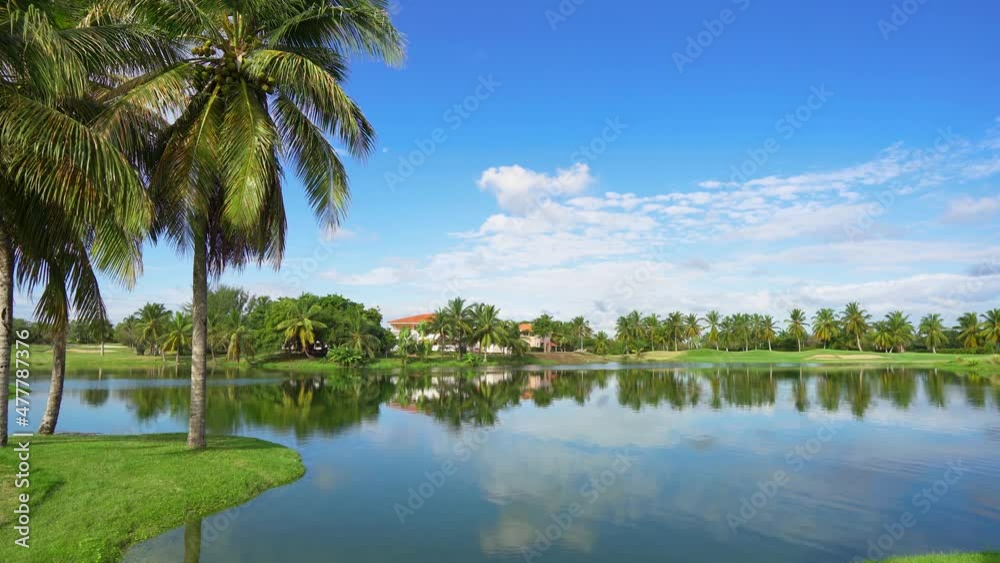 Picturesque tropical landscape with blue mirror lake palm trees and cloudy sky. Short-cut golf courses with sand traps on a sunny summer day in the Dominican Republic. Picturesque tropical landscape with blue mirror lake palm trees and cloudy sky. Short-cut golf courses with sand traps on a sunny summer day in the Dominican Republic.