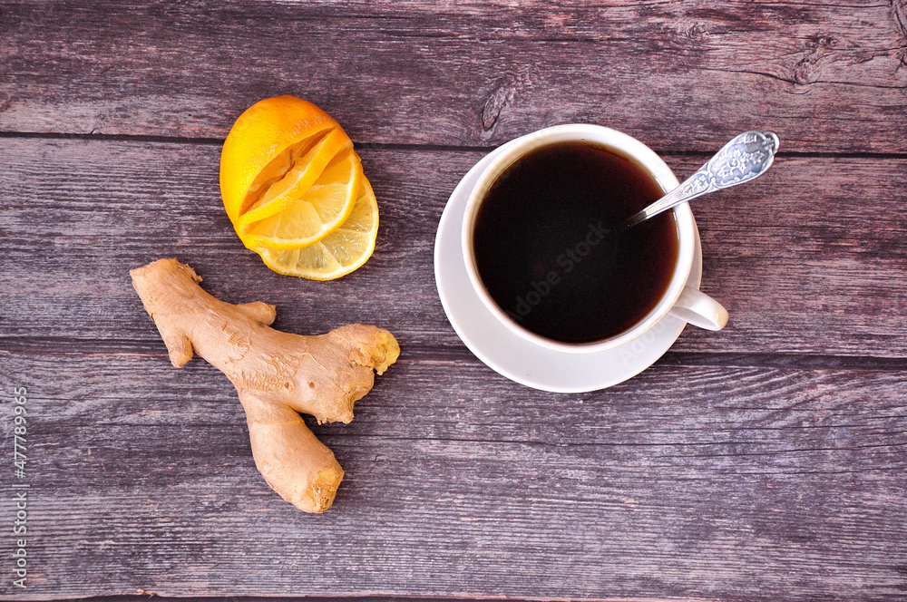 Ginger root, lemon slices and a cup of black tea on a wooden table. Ginger root, lemon slices and a cup of black tea on a wooden table.