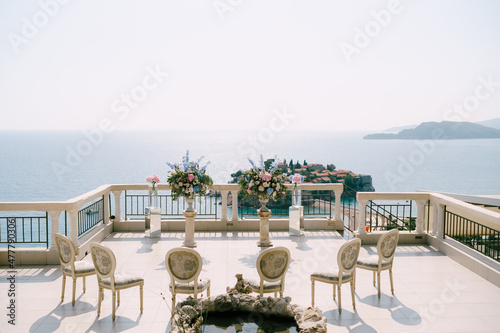 Upholstered chairs stand in front of pedestals with flowers overlooking the Sveti Stefan island 