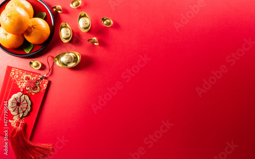 Chinese new year decorations made from red packet, orange and gold ingots or golden lump on a red background. Chinese characters FU in the article refer to fortune good luck, wealth, money flow. © Siam