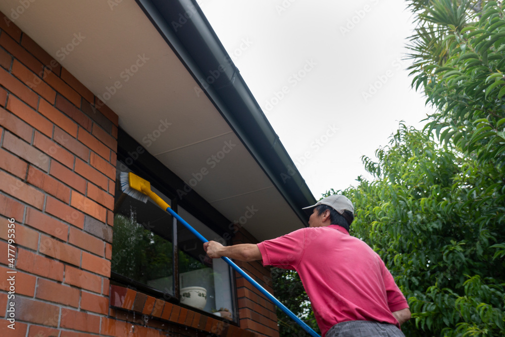 Low angle view of a man washing window with long pole and brush in Auckland