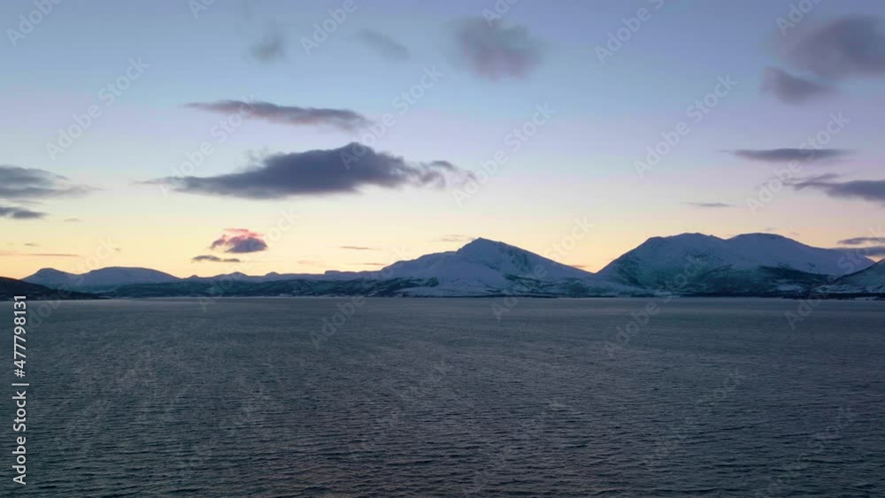 Drone shot flying low over water towards snow-capped mountains at sunset Drone shot flying low over water towards snow-capped mountains at sunset