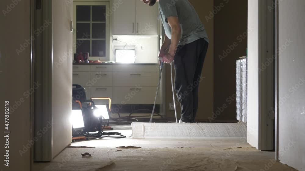 Man sweeping while doing home renovation with many bright lamps Man sweeping while doing home renovation with many bright lamps