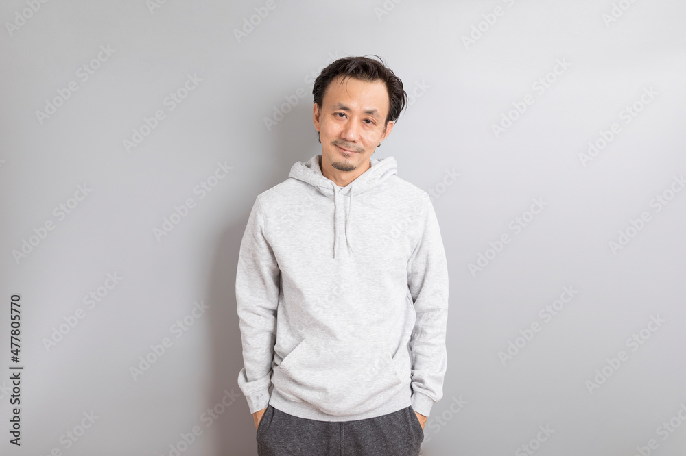 Confident asian man in a hoodie standing on grey background.