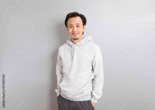Confident asian man in a hoodie standing on grey background. © bennnn