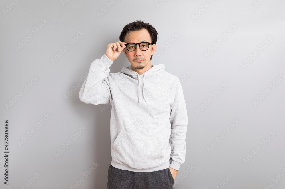 Asian adult man wearing hoodie with eyeglasses standing on grey background.