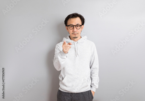 Adult Asian Man in hoodie Wear eyeglasses and Pointing Finger on Gray Background.