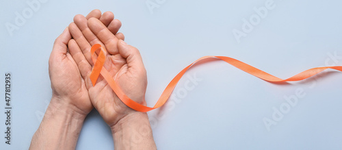Photo Male hands with orange ribbon on light background