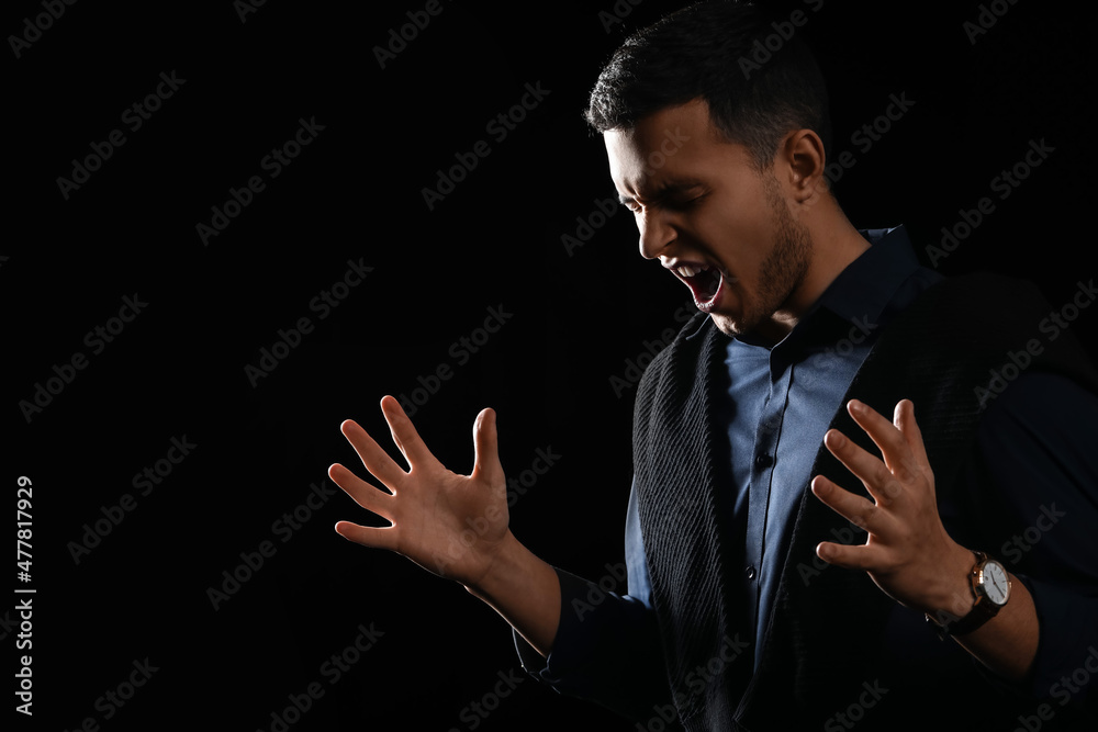 Portrait of screaming young man on black background