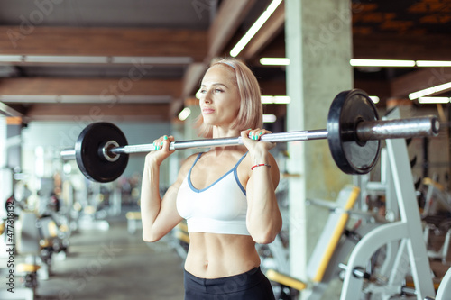 Athletic woman holding barbell in her hands in gym